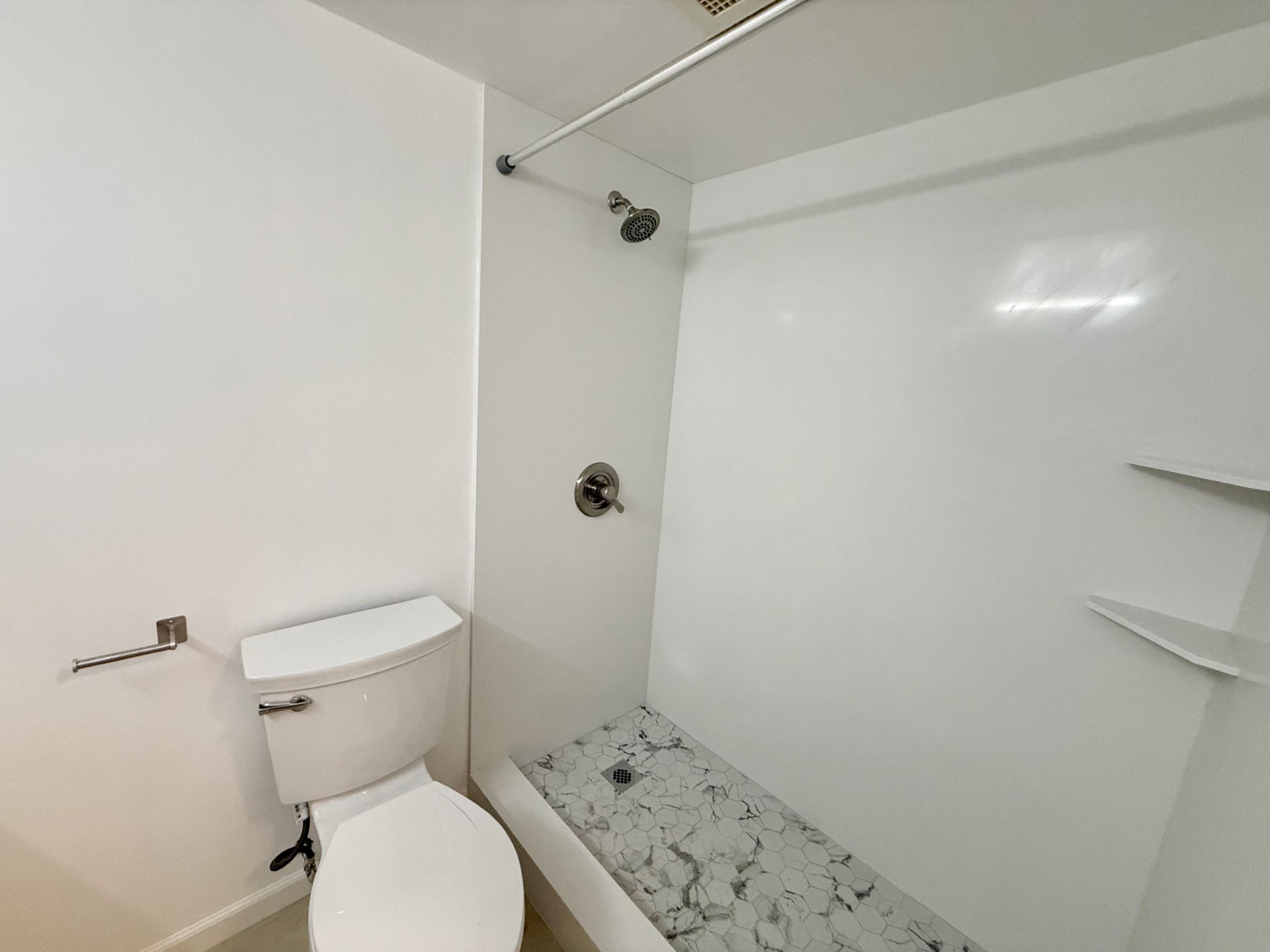 A white toilet is in a small bathroom with a shower.